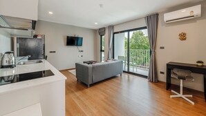 A modern kitchen with a built-in stove, a grey sofa, and a dining area with a black table and chair. - Modern Condo Walk to Rawai Beach C188 (Rawai)