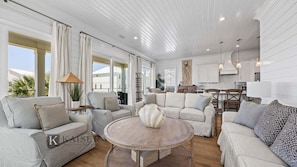 A spacious living room with a large round coffee table, two sofas, and a dining area with a kitchen in the background.