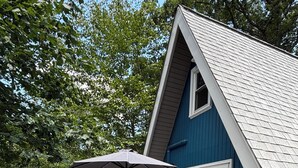 A deck with outdoor furniture and a large umbrella. - Cozy 2-bedroom tiny cabin with roomy loft, AC, and fire pit near Bryce Resort (Mount Jackson)