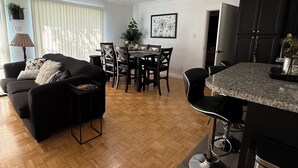 A modern living room with a black sofa, wooden flooring, and a dining area with a table and chairs.