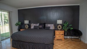 A bedroom with a large bed, two bedside tables, a chair, and a potted plant.