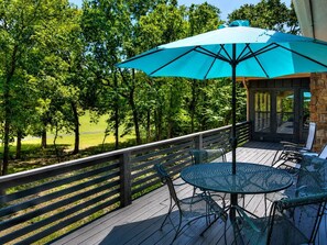 A deck with a table and chairs, a blue umbrella, and a view of trees and grass.