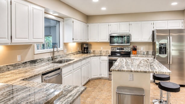 A modern kitchen with white cabinets, granite countertops, stainless steel appliances, and a window providing natural light. - Pool House on Ponce De Leon (Hot Springs)