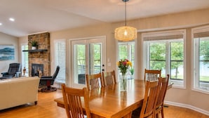 A dining area with a wooden table and chairs, a hanging light fixture, and large windows with a view of greenery. - Pool House on Ponce De Leon (Hot Springs)