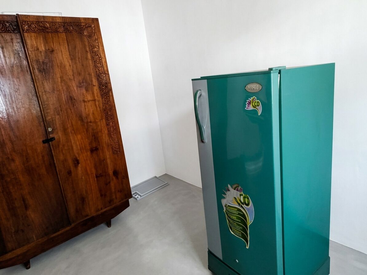 A teal refrigerator with a sticker, a wooden wardrobe, and a white wall.