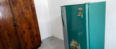 A teal refrigerator with a sticker, a wooden wardrobe, and a white wall.