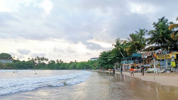 A beach with palm trees, a sign for 'AHIKAVA,' and a lifeguard tower. - The Dutch Inn (Galle)