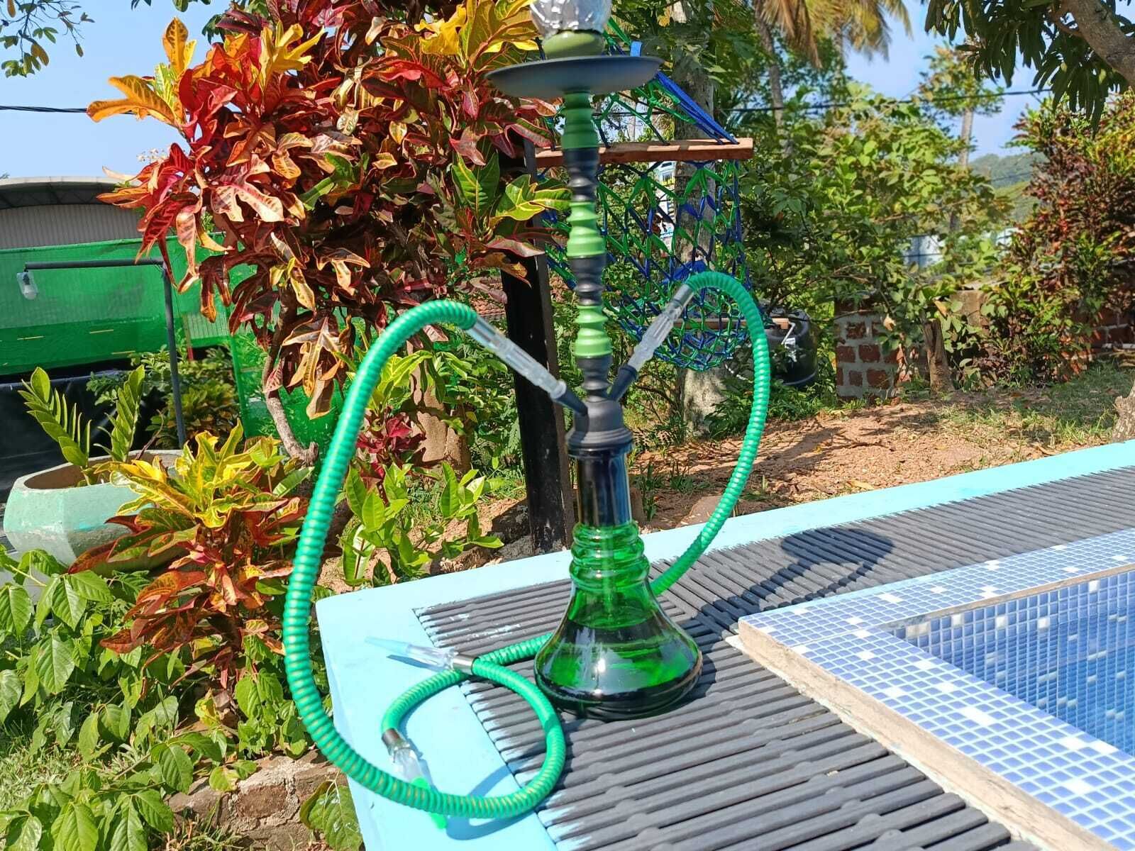 Una shisha sobre una taula a l'exterior, amb un paviment de rajoles i vegetació de fons.
