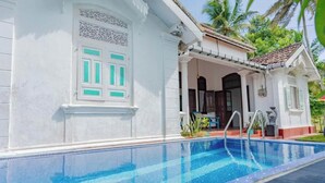 A swimming pool adjacent to a building with a white facade and a door with green accents. - The Dutch Inn (Galle)