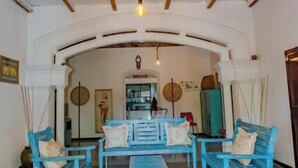 A spacious room with a high ceiling and wooden beams, featuring a central seating area with blue chairs and a bench. - The Dutch Inn (Galle)
