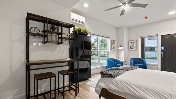 A modern bedroom with a bed, a desk with two stools, a large window, and a balcony.