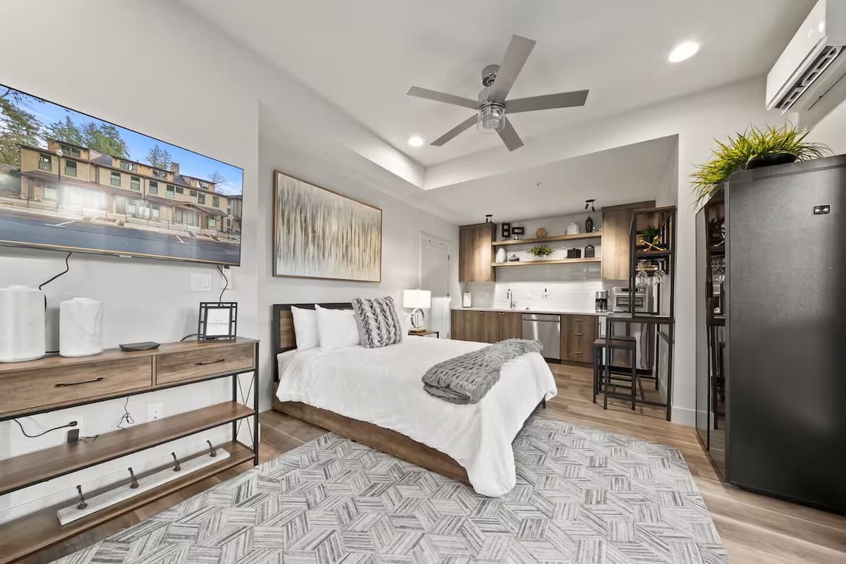 A modern bedroom with a large bed, a ceiling fan, and a view of a cityscape through a window.