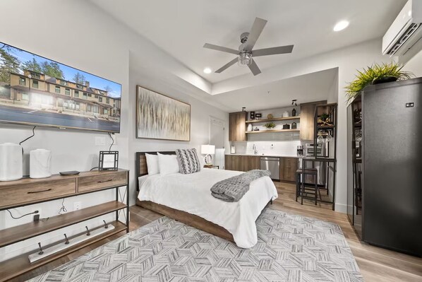 A modern bedroom with a large bed, a ceiling fan, and a view of a cityscape through a window.