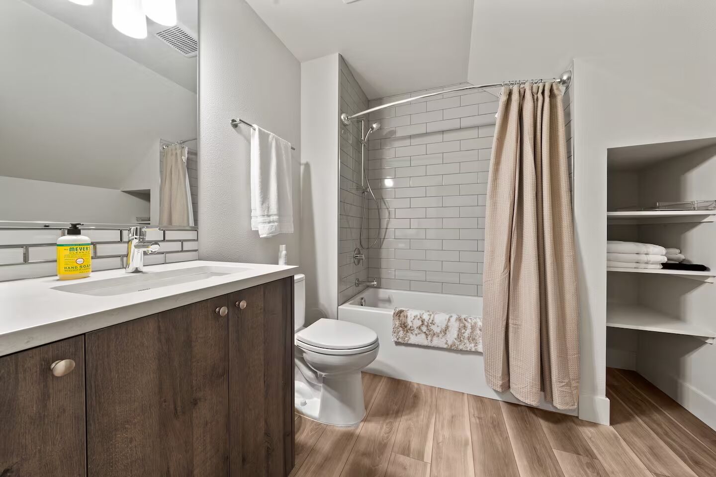 Une salle de bain moderne avec un meuble-lavabo en bois, des toilettes blanches, une baignoire et un rideau de douche.