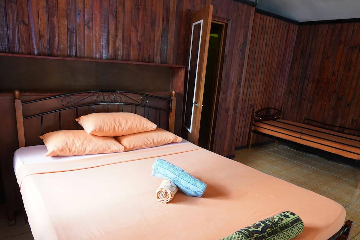 Una cama individual con cabecera de madera, un banco y una puerta en una habitación con paneles de madera.
