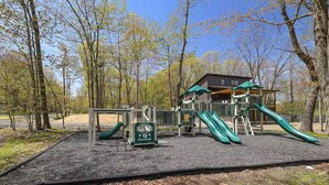 A playground with slides and a small building, surrounded by trees.