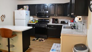 A compact kitchen with dark cabinets, a refrigerator, a microwave, a coffee maker, and a sink.