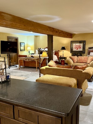 A living room with a sofa, ottoman, TV, and a table with a lamp.