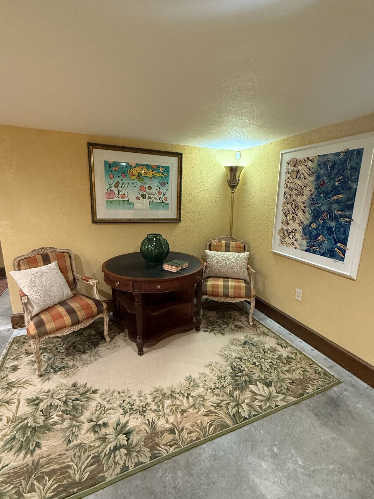 A room with two armchairs, a round table, a floor lamp, and two framed artworks on the walls.