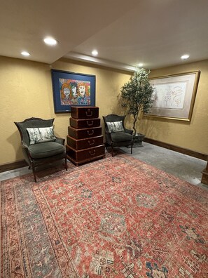 A room with two armchairs, a stack of suitcases, a patterned rug, and artwork on the walls.