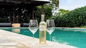 A poolside setting with a bottle of Freixenet wine and two glasses, a covered seating area, and a pool. - Charming King Bedroom - Pool View - Walking Distance to Beach & Golf Course. (Wamberal)