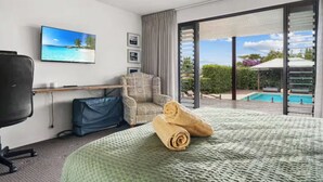 A hotel room with a bed, a chair, a desk, a TV, and a view of a swimming pool. - Charming King Bedroom - Pool View - Walking Distance to Beach & Golf Course. (Wamberal)