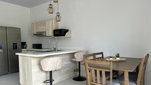 A modern kitchen with a central island, bar stools, a wooden dining table, and a built-in microwave. - Amazing 3-bedroom apartment with AC in Tamarindo (Tamarindo)