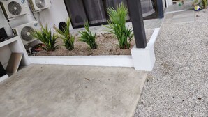 A modern building exterior with multiple air conditioning units, a concrete pathway, and a small garden area with plants. - Amazing 3-bedroom apartment with AC in Tamarindo (Tamarindo)