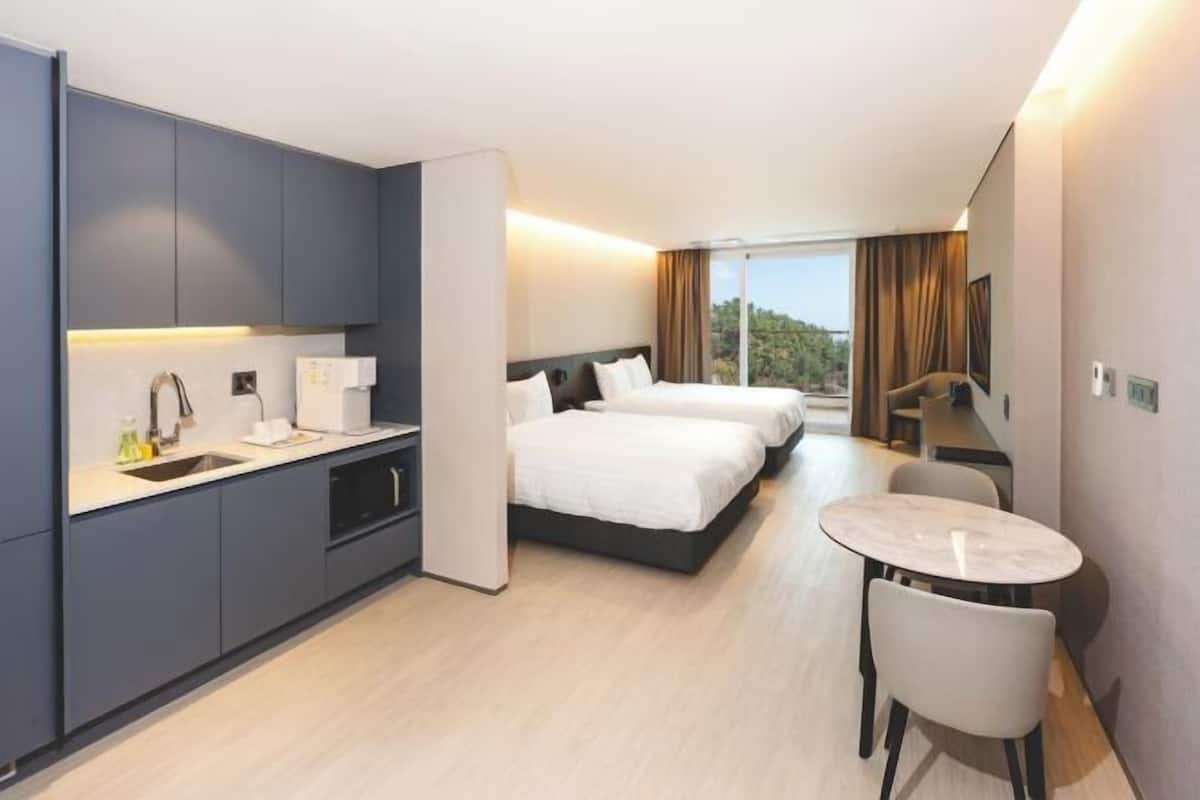 A hotel room with a bed, a small table, a kitchenette, and a view of the outdoors.