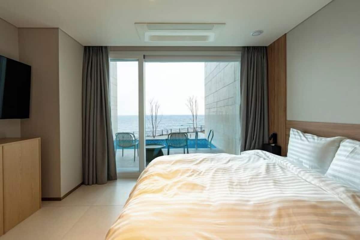 A hotel room with a bed, a television, a desk, and a view of the sea.