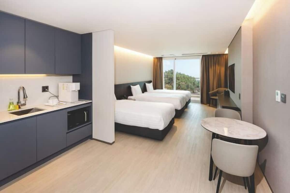 A hotel room with a kitchenette, two beds, a dining table, and a TV.