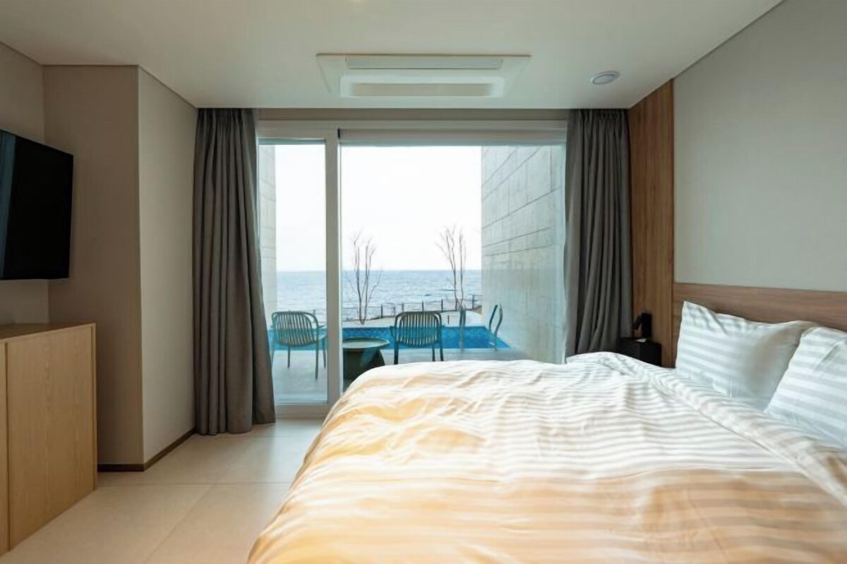 A hotel room with a bed, a television, a desk, and a view of the sea.
