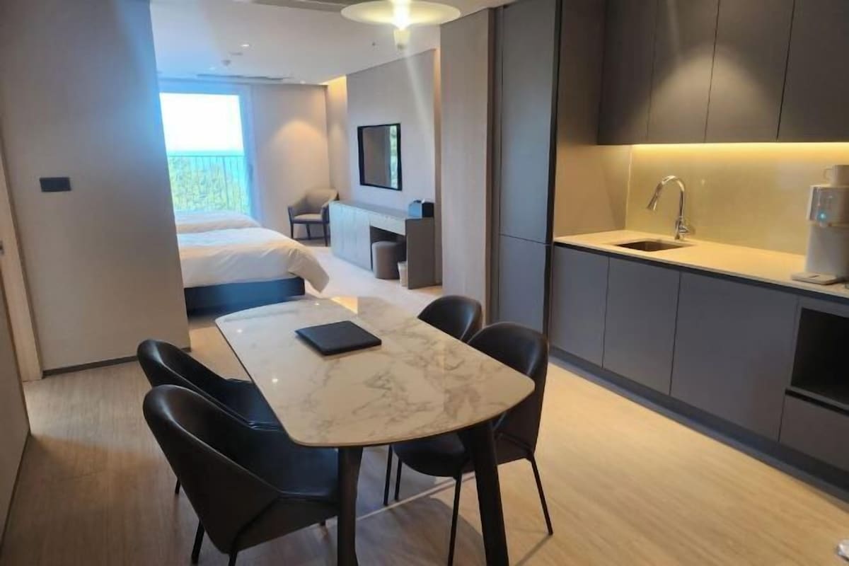 A modern hotel room with a dining area, a bed, a small kitchenette, and a balcony.