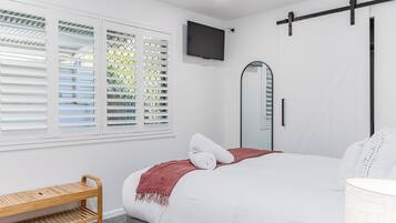 Un dormitorio con una cama, televisión, espejo y una banca.