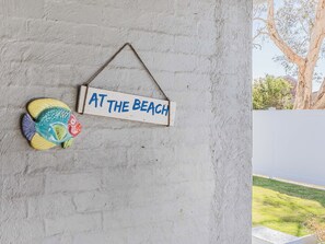 A wall with a hanging sign that reads "AT THE BEACH" and a decorative fish sculpture. - Slow M Ocean Cabarita - Pet Friendly (Bogangar)