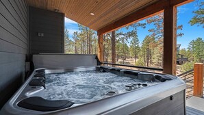 A hot tub with multiple jets, set on a wooden deck with a view of a forested area. - Charming & Luxurious 5-Bedroom Cabin in Heber (Overgaard)