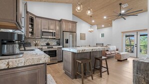A modern kitchen with granite countertops, stainless steel appliances, and a central island with bar stools. - Charming & Luxurious 5-Bedroom Cabin in Heber (Overgaard)