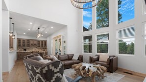 A spacious living area with a large sectional sofa, a unique coffee table, and a view of the kitchen and outdoors. - Charming & Luxurious 5-Bedroom Cabin in Heber (Overgaard)