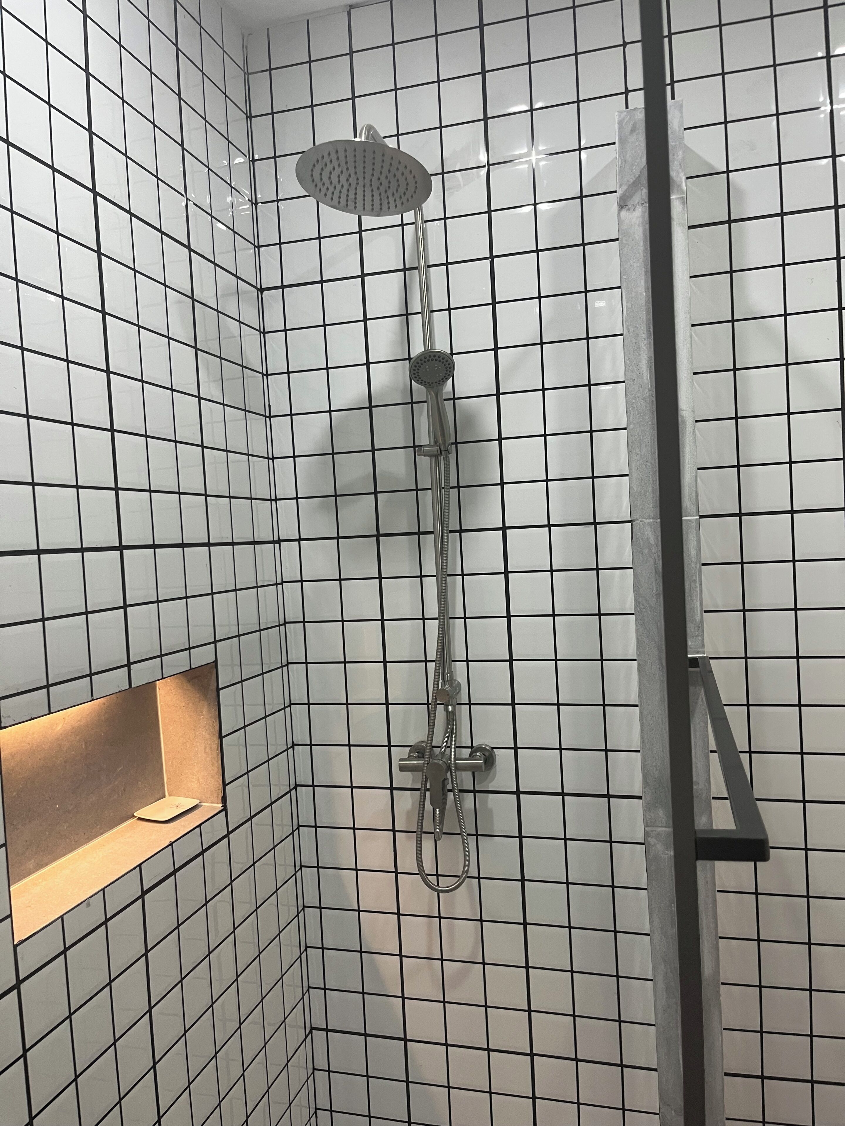 A shower with a handheld showerhead and a wall-mounted faucet.