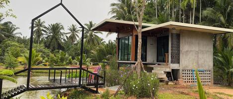 A modern house with a wind turbine, surrounded by lush greenery and a small pond.