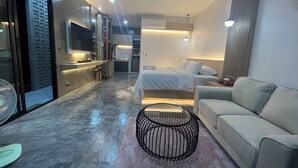 A modern hotel room with a bed, a sofa, a small table, a kitchen area, and a sliding door. - Darisa Home (Surat Thani)