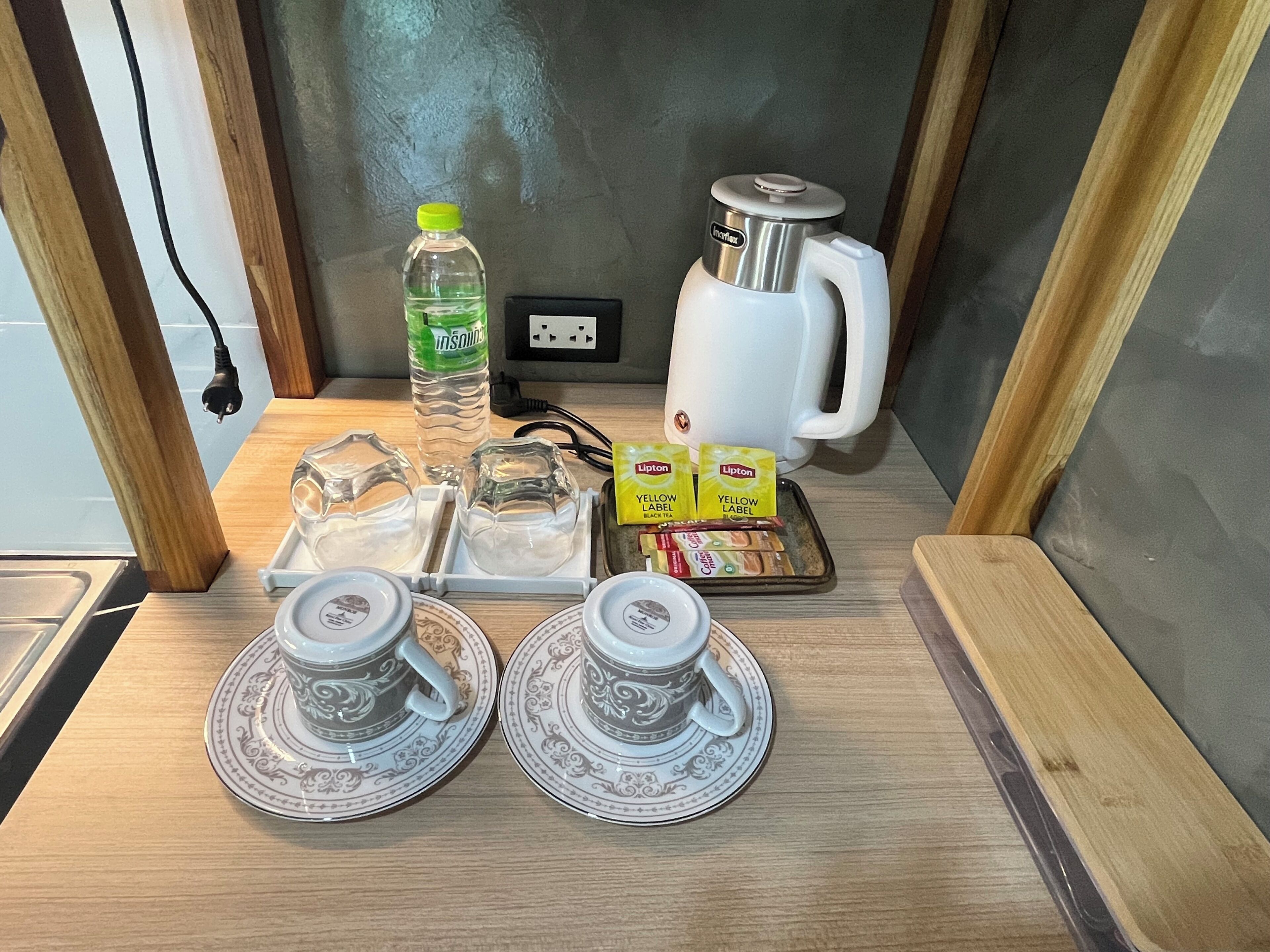 Una encimera de cocina con una tetera, una botella de agua, sobres de té Lipton y dos tazas con platillos.