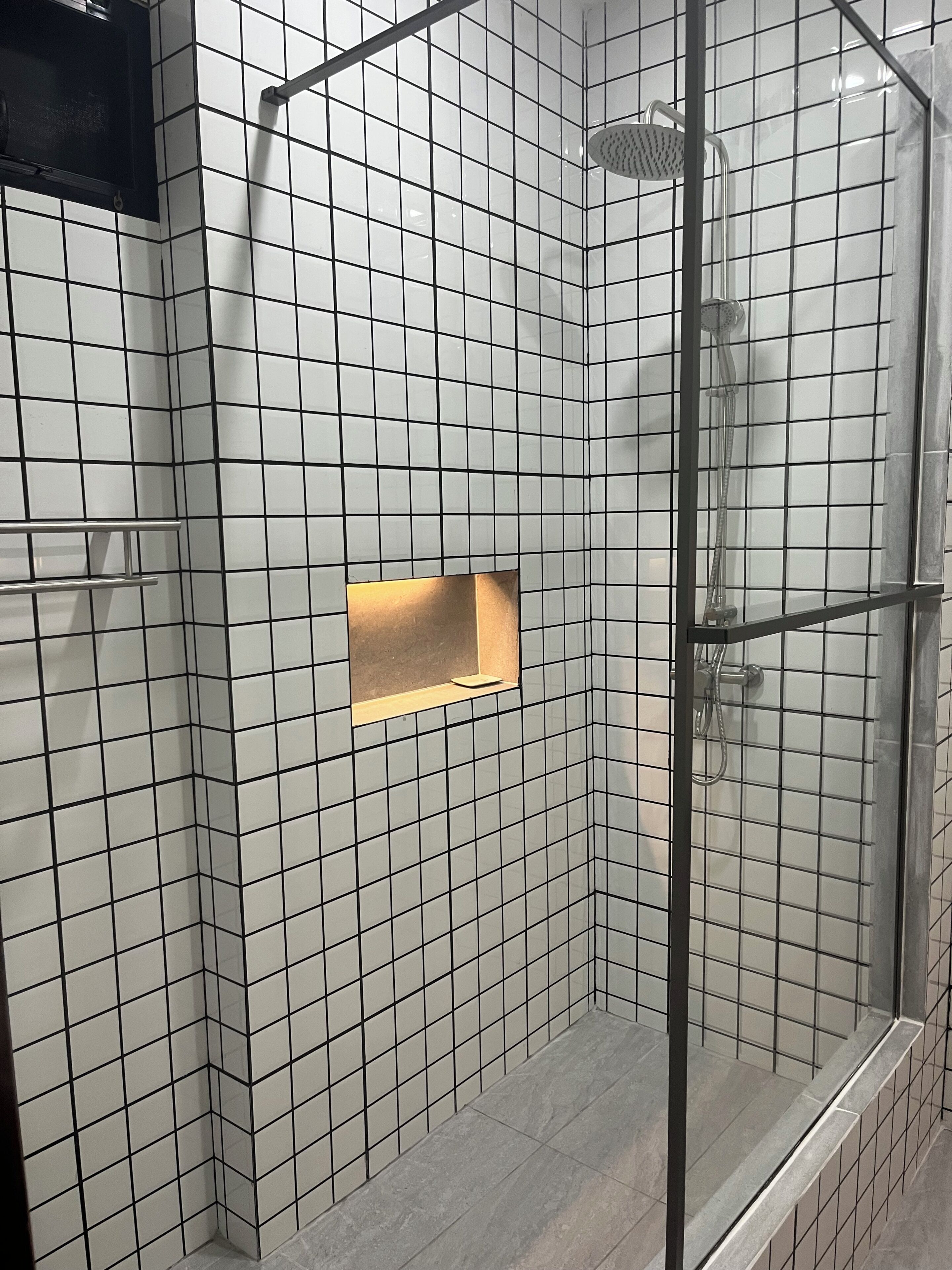 A shower with a glass door, tiled walls, and a small shelf.