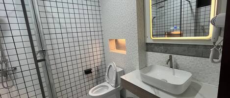 Un baño moderno con ducha, inodoro y lavamanos, que presenta un revestimiento de azulejos y un espejo con marco iluminado.