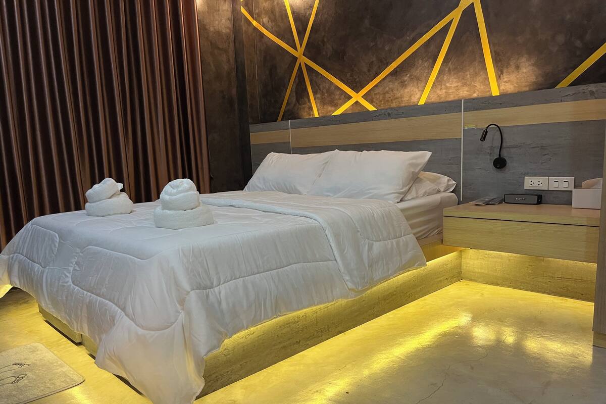 A modern hotel room with a large bed, a bedside table, and a wall with geometric patterns.