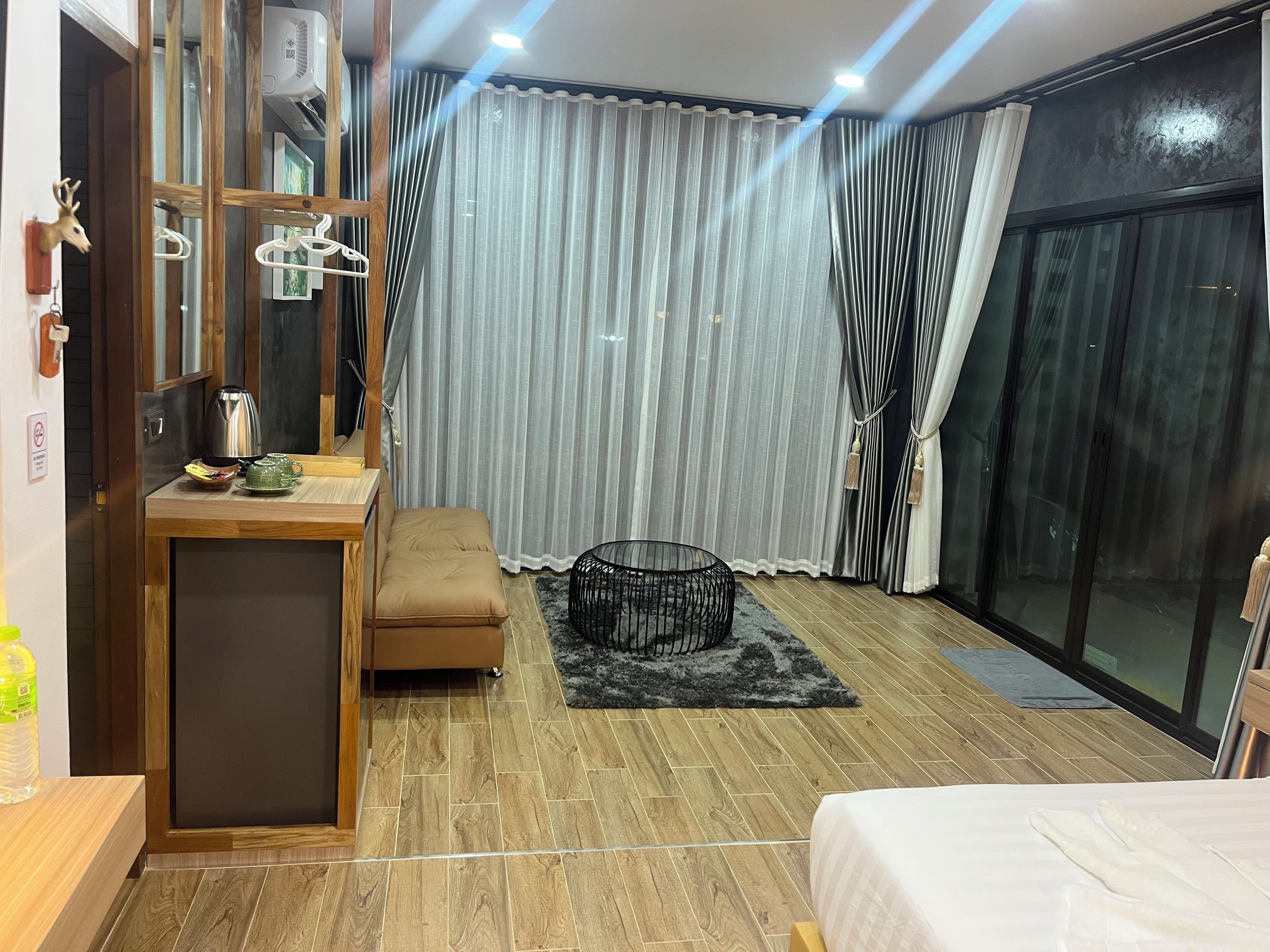 A modern hotel room with a wooden desk, a cushioned bench, a black chair, a bed, and a large sliding glass door.