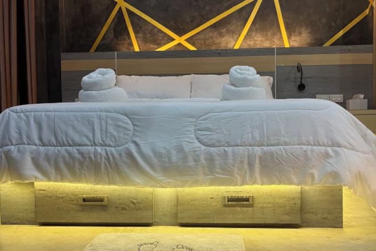 A neatly made bed with white linens and two folded towels at the head.