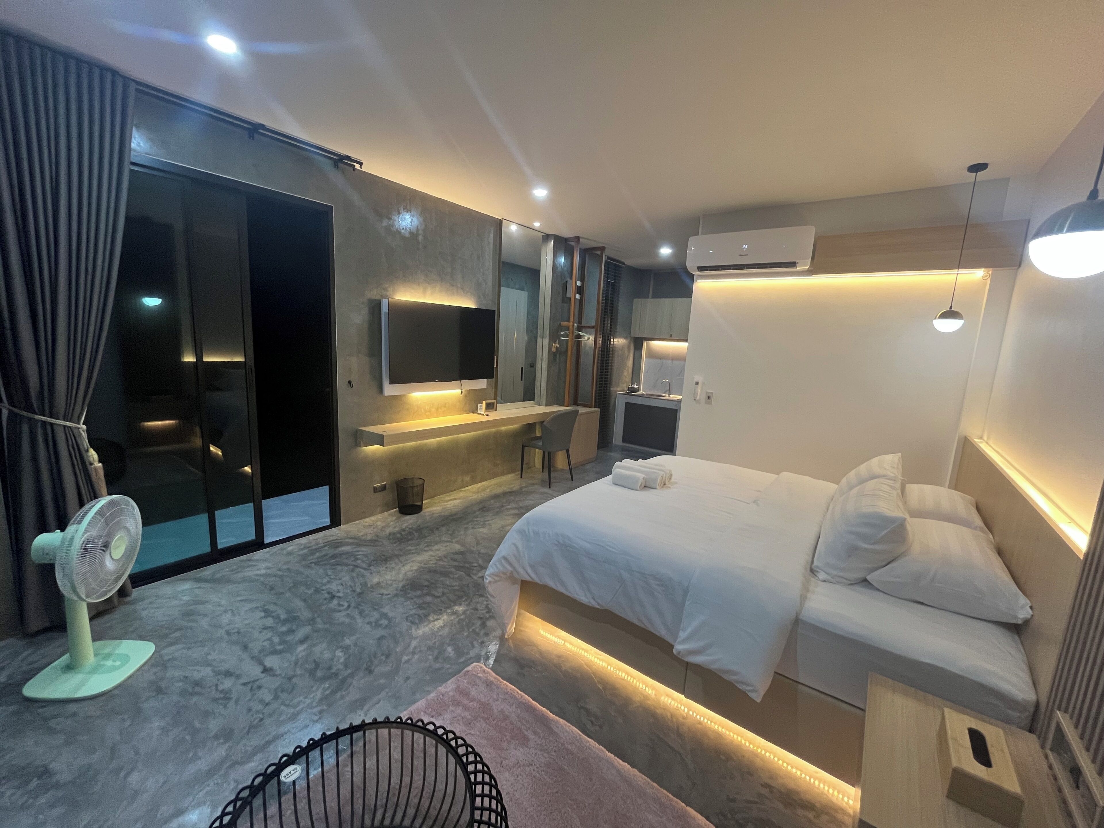 Une chambre d’hôtel moderne avec un grand lit, un bureau, une chaise, une petite table, un miroir et une fenêtre avec des rideaux.