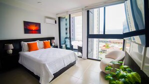 Een moderne hotelkamer met een groot bed, uitzicht op de stad door middel van kamerhoge ramen en een balkon met een stoel en planten.
