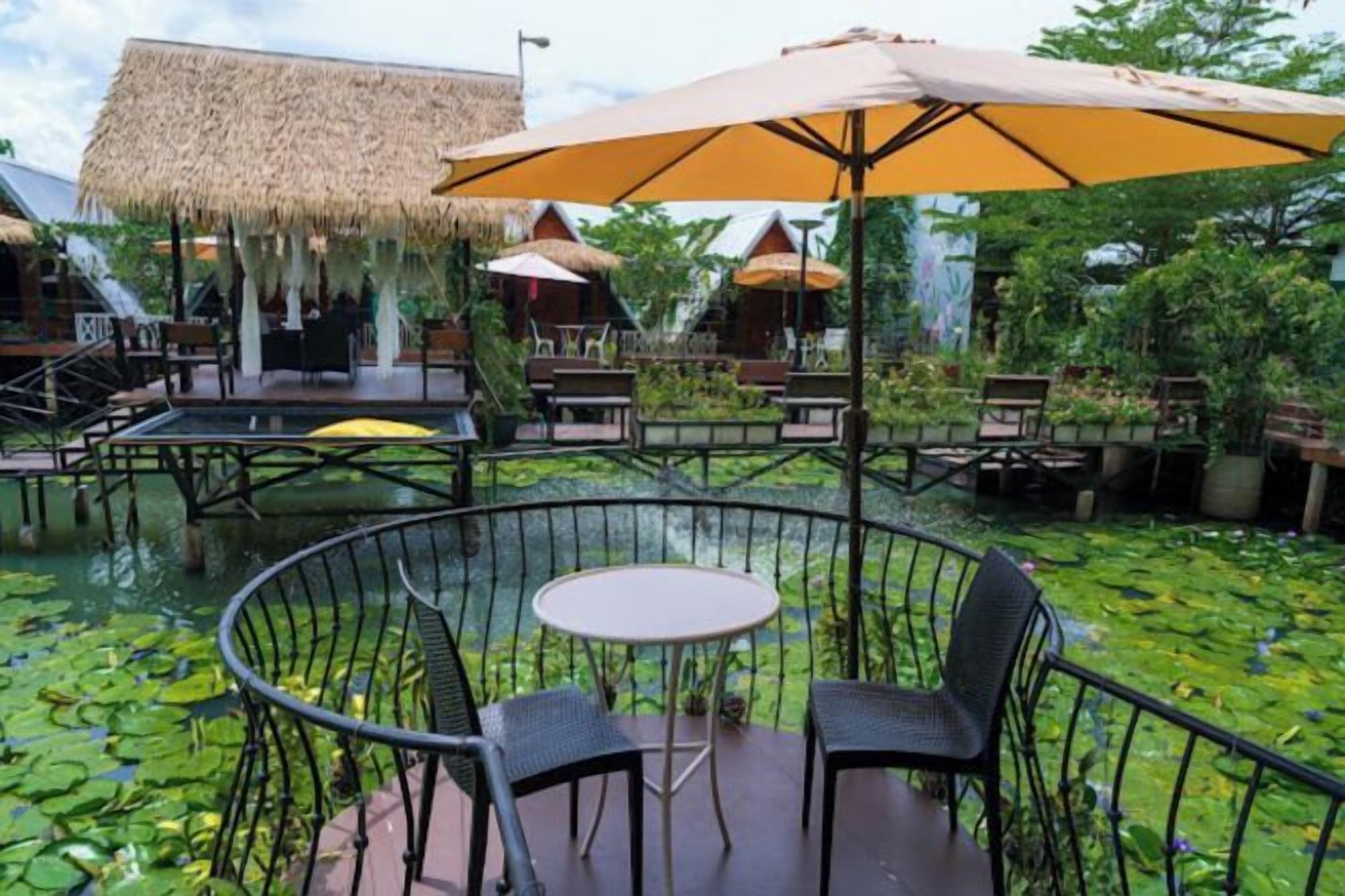 A circular outdoor seating area with a table and chairs, surrounded by a water feature with lily pads.